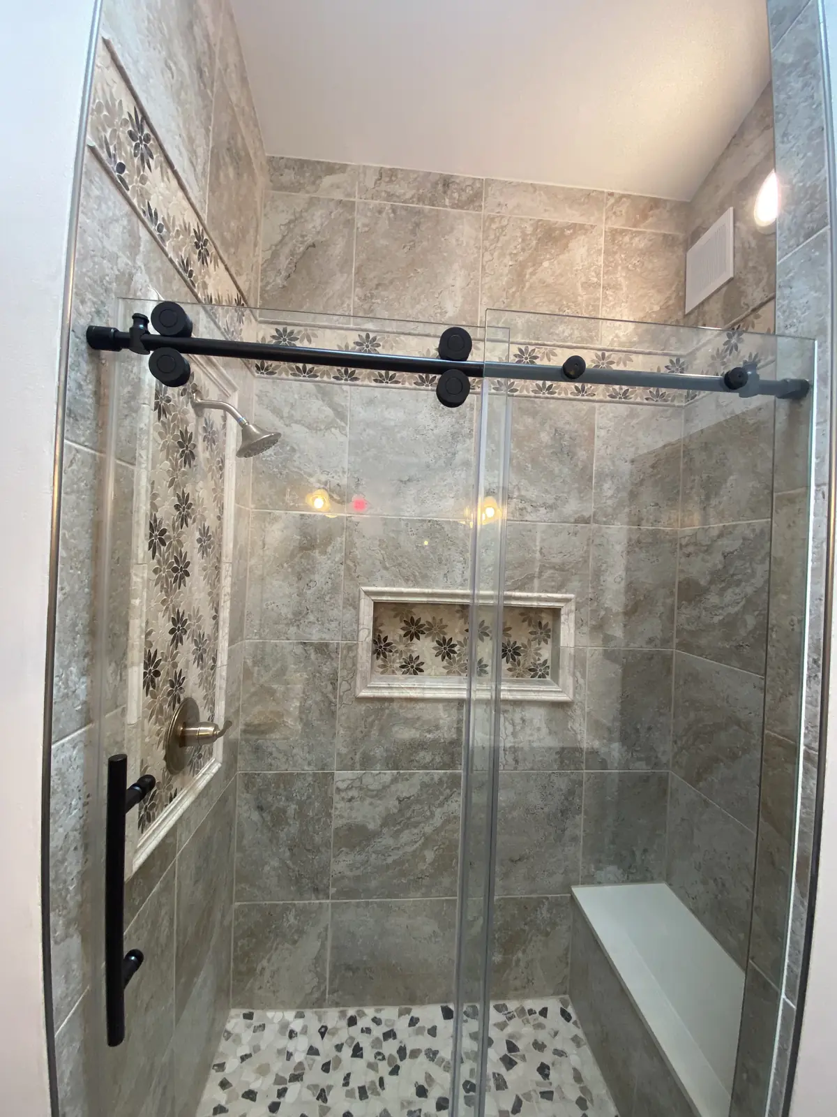 Walk-in shower with earth-tone tile and pebble floor